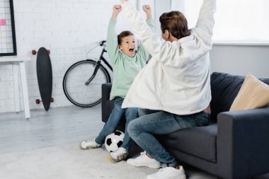 Oğlan ve baba evdeki futbol topunun yanında evet işareti yapıyorlar. 