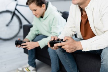 KYIV, UKRAINE - 11 Ekim 2021: Evde bulanık bir çocuğun yanında joystickli bir adam video oyunu oynuyor 