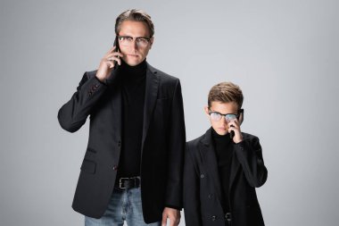 Oğlan ve baba ceketli. Griler üzerinde izole edilmiş akıllı telefonlardan konuşuyorlar. 