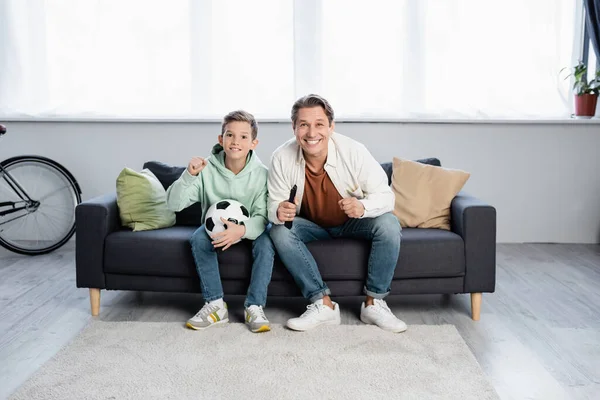Excited father and son with football ball watching movie at home
