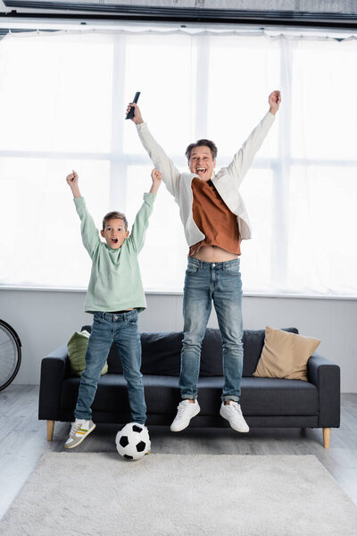 Excited family with remote controller jumping near football ball at home 