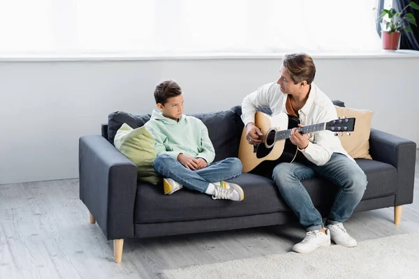 Homme Jouant Guitare Acoustique Près Bouleversé Enfant Sur Canapé — Photo