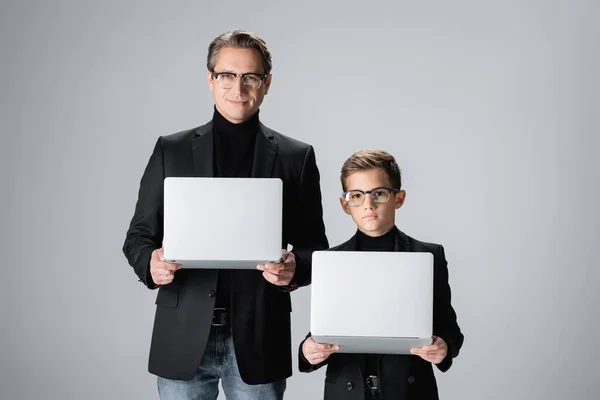 时尚的十多岁的儿子在家里抱着笔记本电脑 与爸爸隔离在灰色的家中 — 图库照片