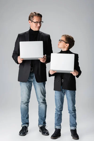 Jongen Jas Holding Laptop Kijken Naar Vader Grijze Achtergrond — Stockfoto