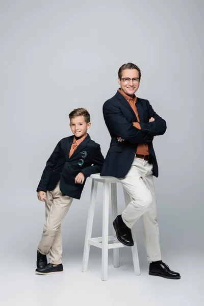 ポジティブでスタイリッシュな父と息子ポーズ近く椅子上のグレーの背景 — ストック写真