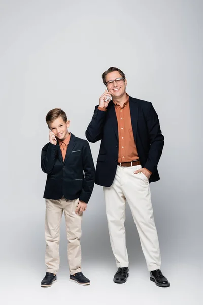 陽気でスタイリッシュな父親と息子は灰色の背景にスマートフォンで話しています — ストック写真