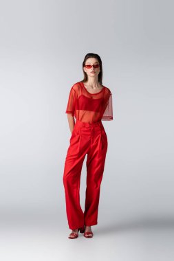 Tam boy güneş gözlüklü genç model ve gri üzerine kırmızı moda poz