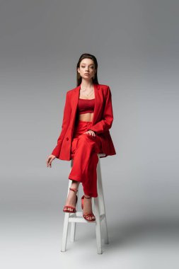 Kırmızı takım elbiseli güzel bir kadın ve koyu gri sandalyede oturan beyaz ayakkabılar.