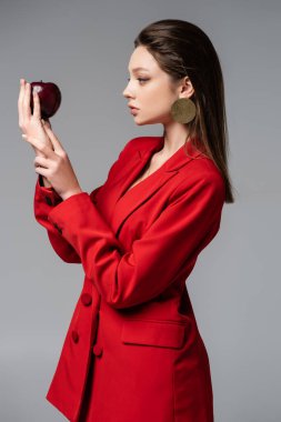 Kırmızılı genç kadın, gri üzerine izole edilmiş elmaya bakıyor. 