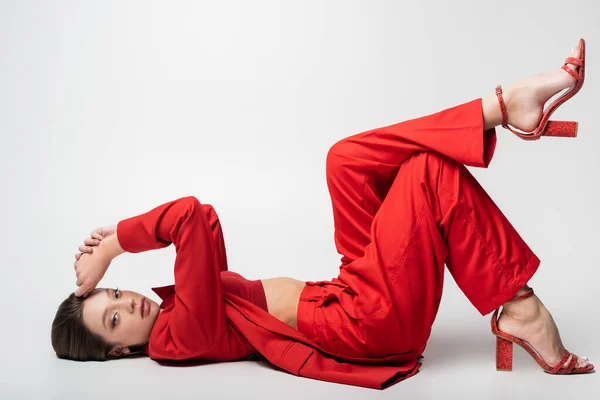 Gri Üzerine Uzanmış Kırmızı Elbiseli Modaya Uygun Genç Bir Kadın — Stok fotoğraf