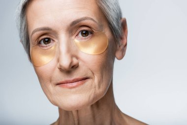 Gri üzerine izole edilmiş göz bantlı orta yaşlı kadının yakın görüntüsü