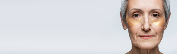 крупным планом женщины средних лет в коллагеновых глазных повязках, смотрящей на камеру, изолированную на сером, баннер