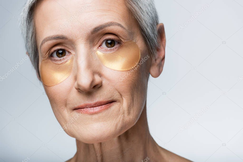 close up view of middle aged woman in eye patches isolated on grey