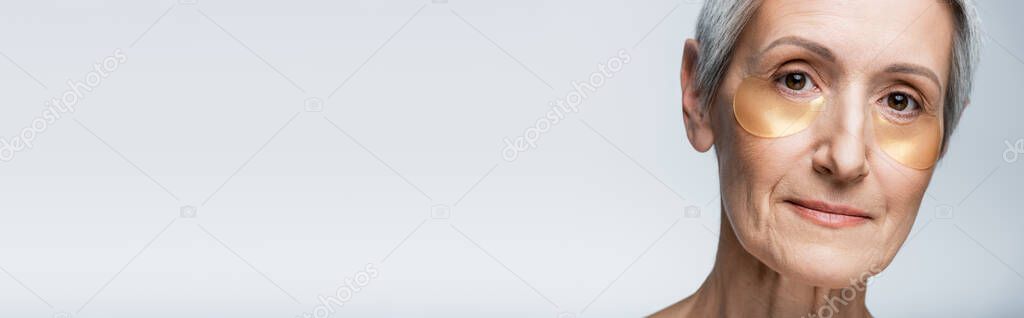 close up view of middle aged woman in eye patches isolated on grey, banner