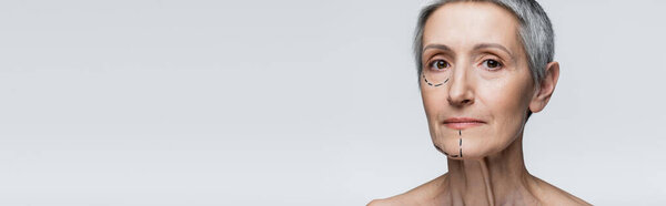 mature woman with wrinkles and marked lines on face looking at camera isolated on grey, banner