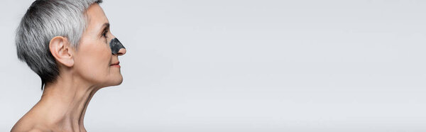 side view of smiling and mature woman with black patch on nose isolated on grey, banner