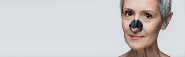 close up of happy middle aged woman with black patch on nose isolated on grey, banner