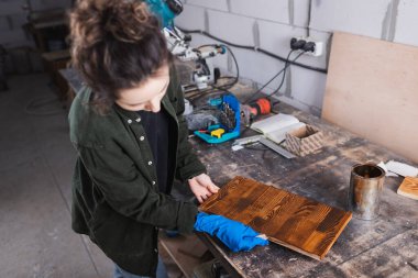 Carpenter applying wood stain on plank in workshop  clipart