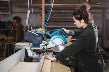 Atölyede testereyle çalışan dövmeli marangozun yan görünüşü 