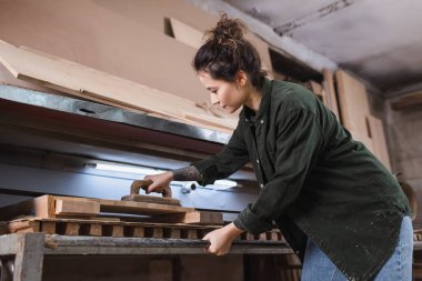 Esmer marangozun atölyede tahta cilalarkenki yan görüntüsü 