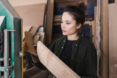 Atölyede tahta tutan gömlekli genç mobilya tasarımcısı. 