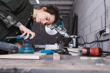 Carpenter using sander on wooden plank in workshop  clipart