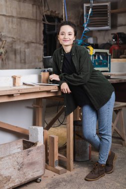 Gülümseyen marangoz atölyeye gitmek için cihazların yanındaki kameraya ve kahveye bakıyor. 