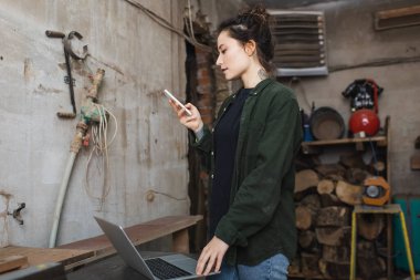 Atölyede cep telefonu kullanan dövmeli ahşap işçisinin yan görünüşü 