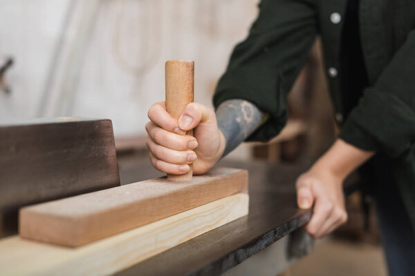 Cropped view of tattooed craftswoman working with plank and jointer machine