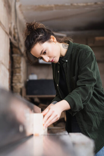 Tattooed furniture designer holding blurred plank near jointer machine