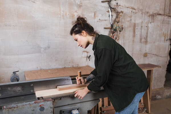 Side view of carpenter working with plank and jointer machine in workshop 