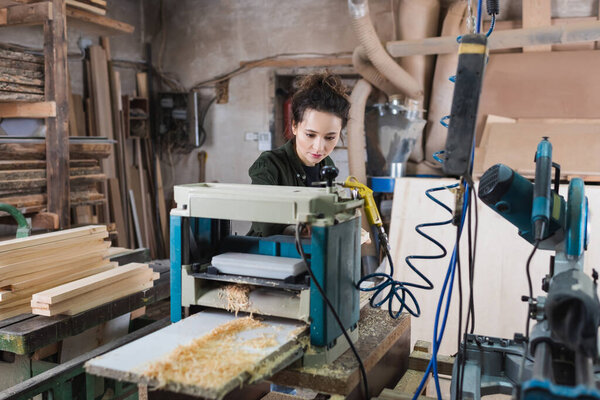 Carpenter working on thickness planer near sawdust in workshop 