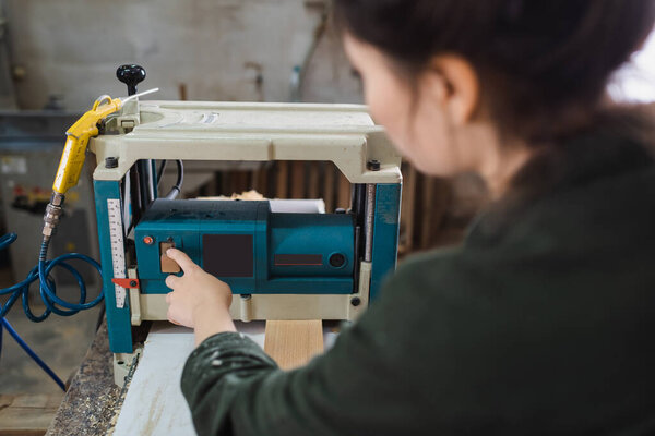 Blurred furniture designer using bench thicknesser near wooden plank in workshop 