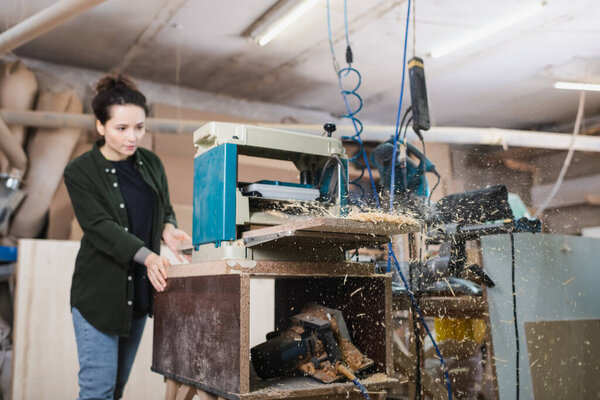 Sawdust and bench thicknesser near blurred carpenter working in workshop 