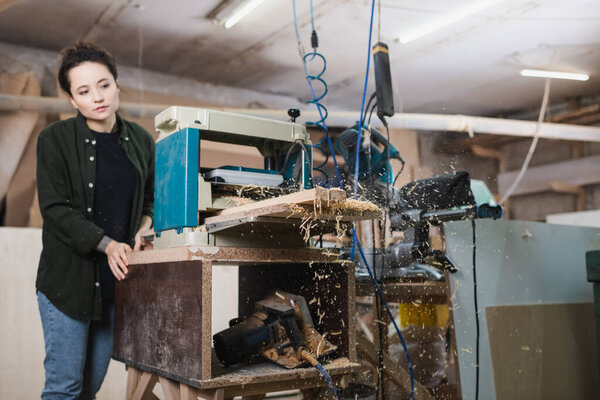 Sawdust and wooden boards in thickness planer near woodworker in workshop 
