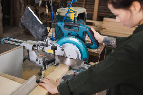Blurred woodworker using miter saw in workshop 