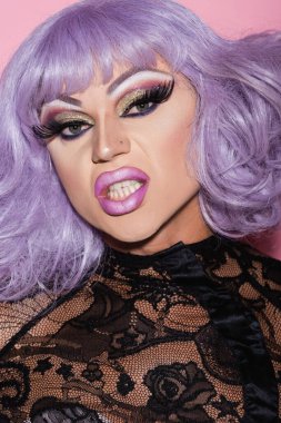 Siyah dantelli ve mor peruklu travesti pembeye bürünmüş.