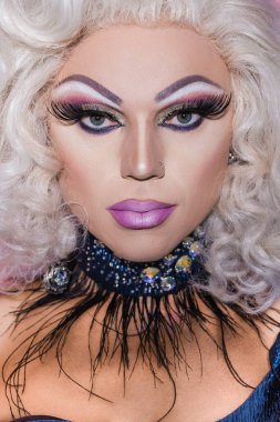Muhteşem makyajlı, peruklu ve parıltılı kolyeli travesti portresi.