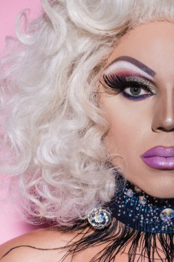 Parlak makyajlı kırpılmış travesti portresi pembeye bakıyor.