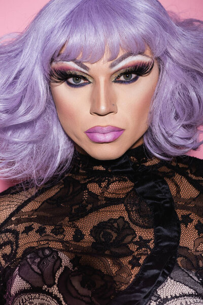 портрет трансвестита в фиолетовом парике, смотрящего на камеру, изолированную на розовом