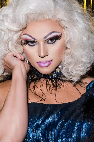 portrait of drag queen in blonde wig and bright makeup looking at camera