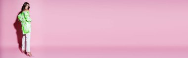 Pembe pankartta poz veren şık giyinmiş esmer bir kadın.