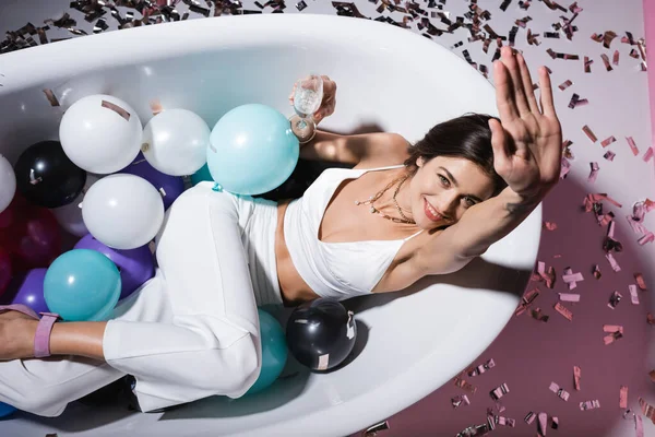 シャンパンのグラスを持ちながら風船で浴槽の中に横になってジェスチャーで前向きな女性のトップビュー — ストック写真