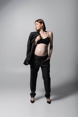 Genç hamile manken gri arka planda spor ceket tutuyor.