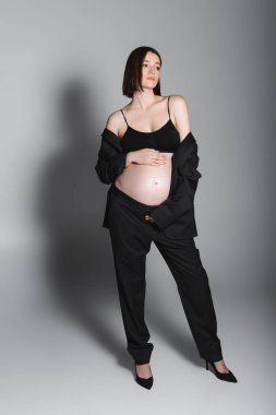 Gri arka planda tam boy hamile model göbeğine dokunuyor. 