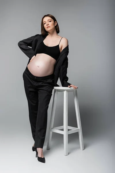 Jonge Zwangere Vrouw Pak Hakken Poseren Buurt Stoel Grijze Achtergrond — Stockfoto