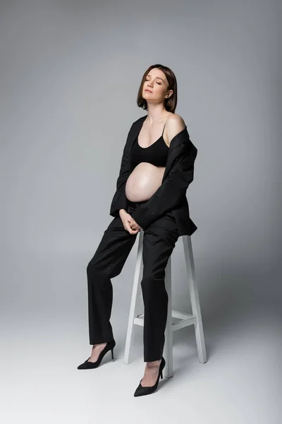Zwanger Model Pak Sluiten Ogen Terwijl Zitten Stoel Grijze Achtergrond — Stockfoto