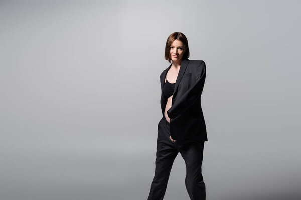 Брюнетка беременная женщина в пиджаке смотрит на камеру, изолированную от серых