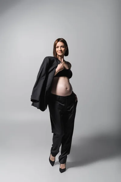 Χαμογελώντας Έγκυος Γυναίκα Στην Κορυφή Κρατώντας Σακάκι Γκρι Φόντο — Φωτογραφία Αρχείου