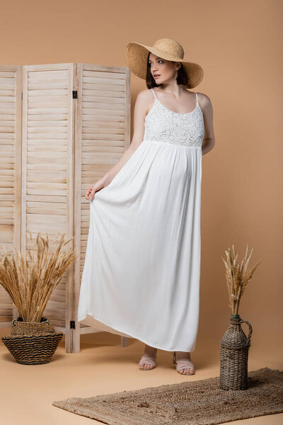 Модная беременная женщина в платье позирует рядом с шипами на бежевом 